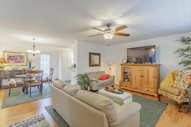 living area featuring light wood-style flooring, ceiling fan with notable chandelier, and a textured ceiling