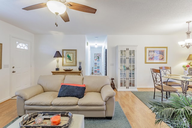 living room with light wood-style flooring, ceiling fan with notable chandelier, and baseboards