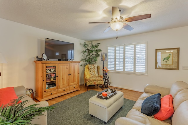 living area featuring baseboards, a textured ceiling, ceiling fan, and light wood finished floors