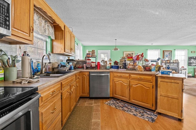 kitchen featuring tasteful backsplash, light countertops, appliances with stainless steel finishes, a peninsula, and a sink