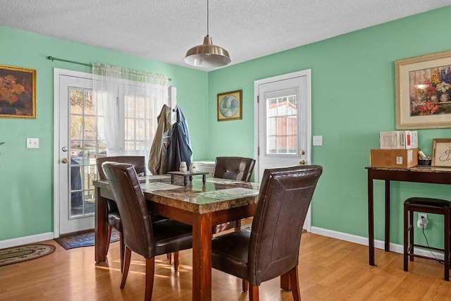 dining room with baseboards, light wood-type flooring, and a textured ceiling