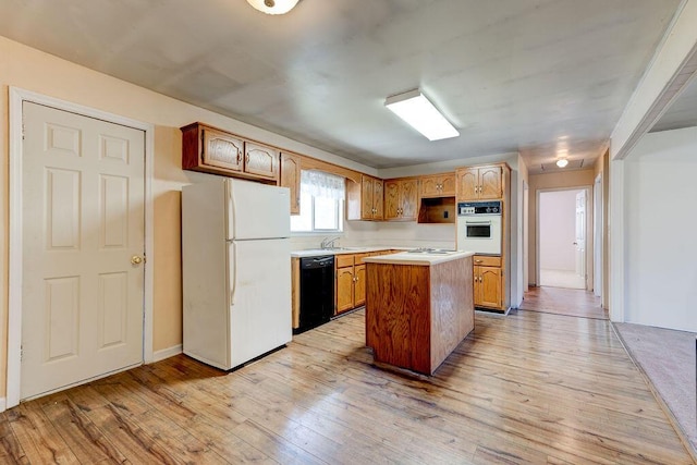 kitchen featuring a kitchen island, light wood-type flooring, light countertops, white appliances, and a sink