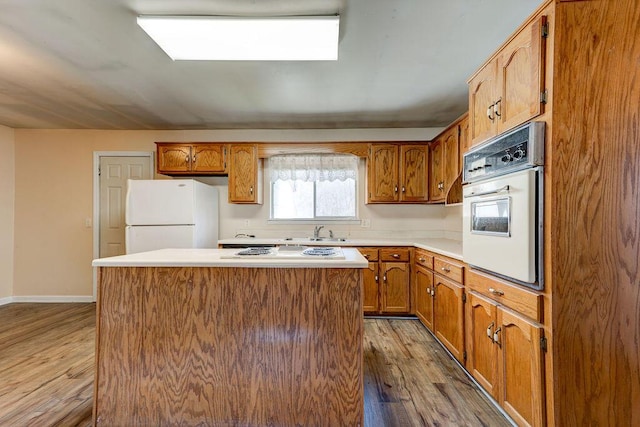 kitchen with a kitchen island, wood finished floors, brown cabinetry, white appliances, and a sink