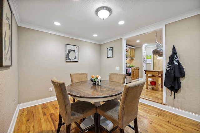 dining space with light wood-type flooring, crown molding, and baseboards