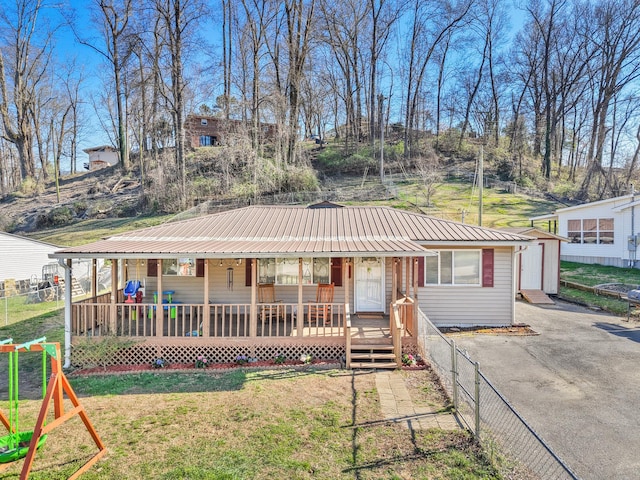 view of front of house featuring driveway, fence, covered porch, a front yard, and metal roof