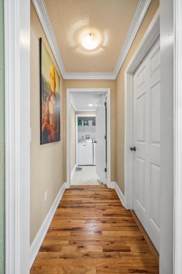 hall featuring baseboards, washing machine and clothes dryer, ornamental molding, light wood-style floors, and a textured ceiling