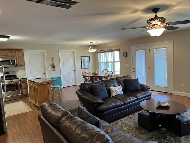 living room featuring visible vents, a ceiling fan, dark wood-style flooring, and baseboards