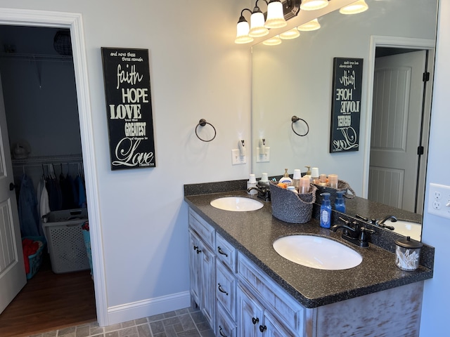 bathroom with double vanity, a spacious closet, baseboards, and a sink