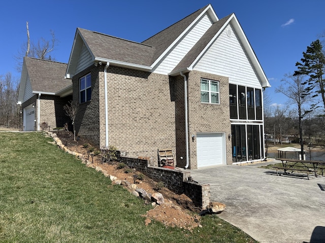 view of side of home with brick siding, a lawn, driveway, a sunroom, and an attached garage