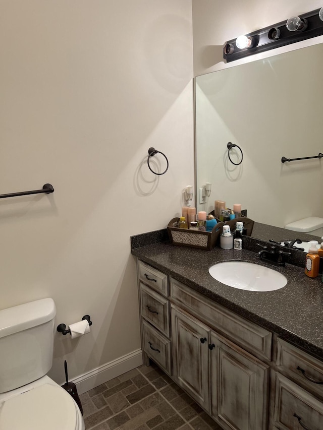 half bathroom with baseboards, toilet, and vanity