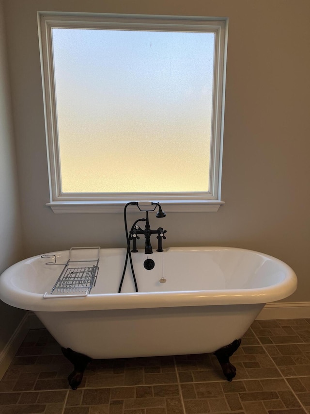 full bath featuring a soaking tub, plenty of natural light, and baseboards