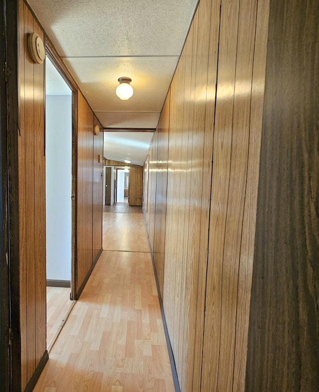 corridor featuring wooden walls, light wood-type flooring, and a textured ceiling