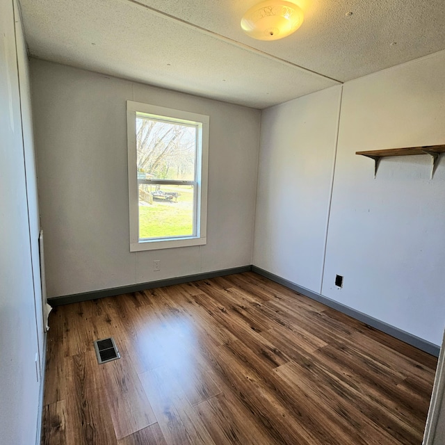 empty room with visible vents, a textured ceiling, baseboards, and wood finished floors