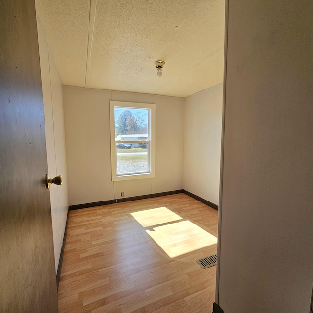 empty room with visible vents, light wood-type flooring, and baseboards