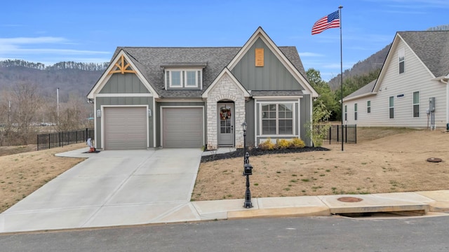 view of front of home featuring fence, a shingled roof, concrete driveway, stone siding, and board and batten siding