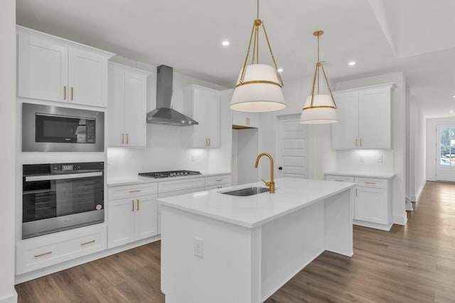 kitchen with dark wood finished floors, a sink, appliances with stainless steel finishes, white cabinetry, and wall chimney exhaust hood