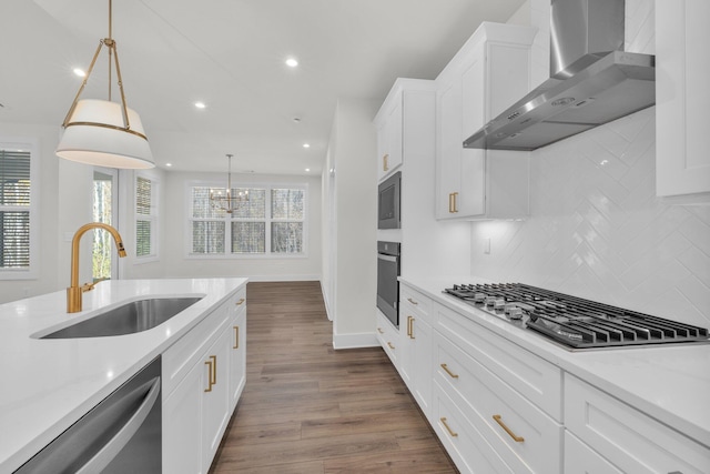 kitchen with dark wood finished floors, appliances with stainless steel finishes, white cabinetry, wall chimney exhaust hood, and a sink