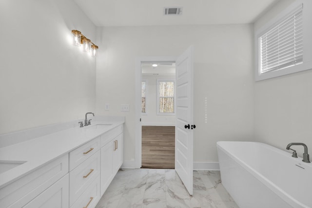 full bath with baseboards, a soaking tub, double vanity, a sink, and marble finish floor