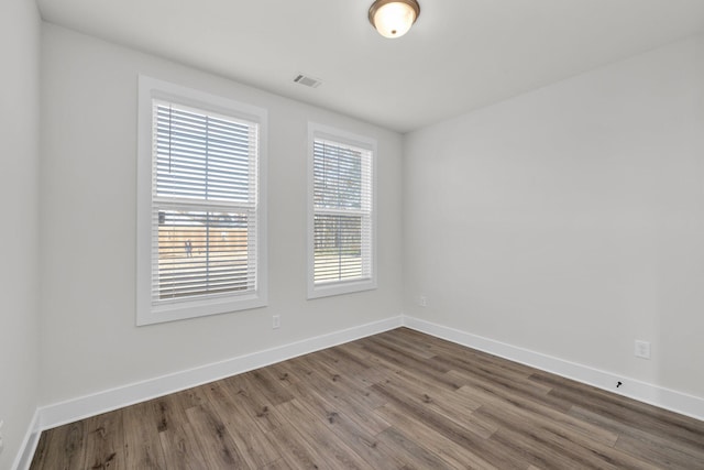 unfurnished room featuring wood finished floors, visible vents, and baseboards