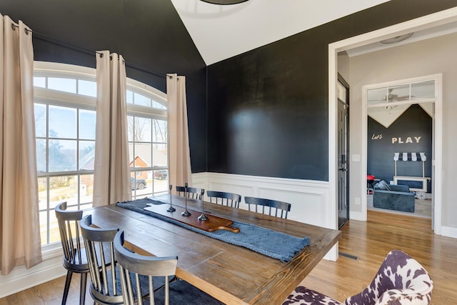 dining space featuring vaulted ceiling, wood finished floors, and a wainscoted wall