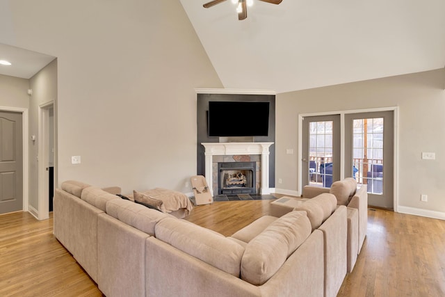 living room featuring baseboards, a ceiling fan, light wood-type flooring, and a tile fireplace