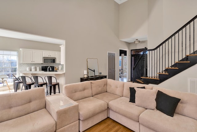 living room with a towering ceiling, light wood-style flooring, and stairs