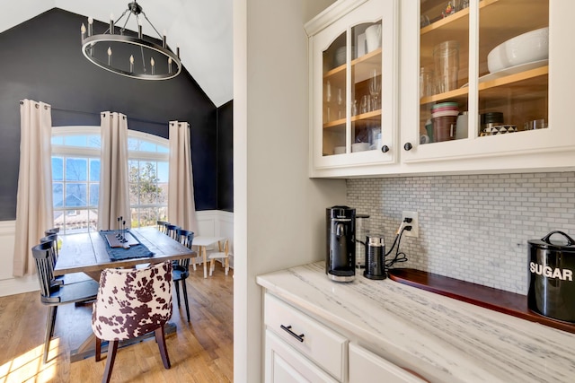 dining space featuring vaulted ceiling, light wood-style flooring, a notable chandelier, and wainscoting