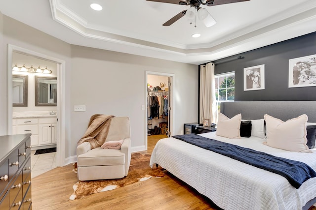 bedroom with a walk in closet, a raised ceiling, light wood finished floors, and ornamental molding