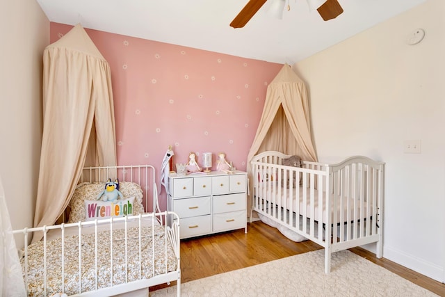 bedroom with a crib, a ceiling fan, baseboards, and wood finished floors