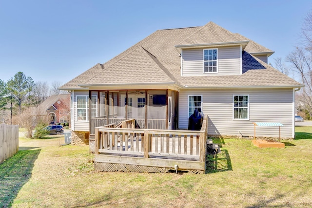 rear view of house featuring a shingled roof, a lawn, a wooden deck, and a sunroom