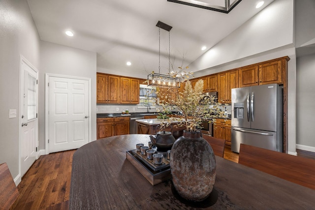 kitchen featuring brown cabinets, dark countertops, dark wood finished floors, appliances with stainless steel finishes, and lofted ceiling