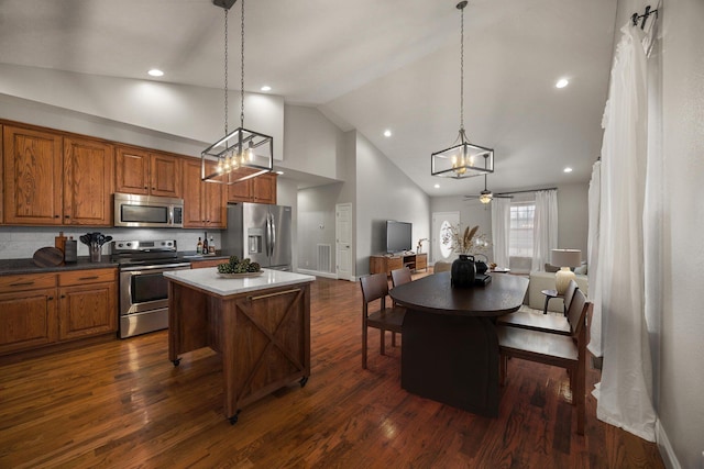 kitchen with brown cabinets, a ceiling fan, a center island, appliances with stainless steel finishes, and dark wood-style flooring