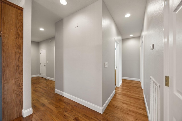 hall with visible vents, baseboards, and light wood finished floors