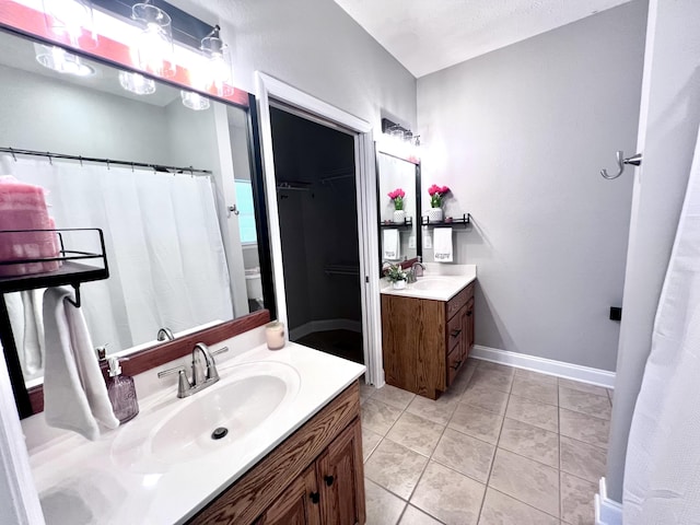 bathroom featuring baseboards, two vanities, a sink, a walk in closet, and tile patterned floors