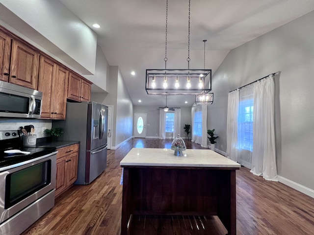 kitchen featuring light stone countertops, decorative light fixtures, brown cabinets, stainless steel appliances, and dark wood-style flooring