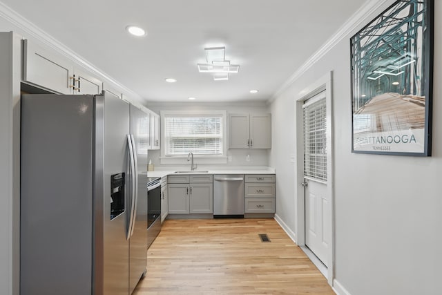 kitchen with light wood-type flooring, ornamental molding, gray cabinets, a sink, and stainless steel appliances