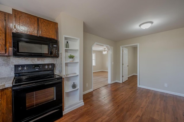 kitchen with baseboards, brown cabinets, dark wood-type flooring, and black appliances