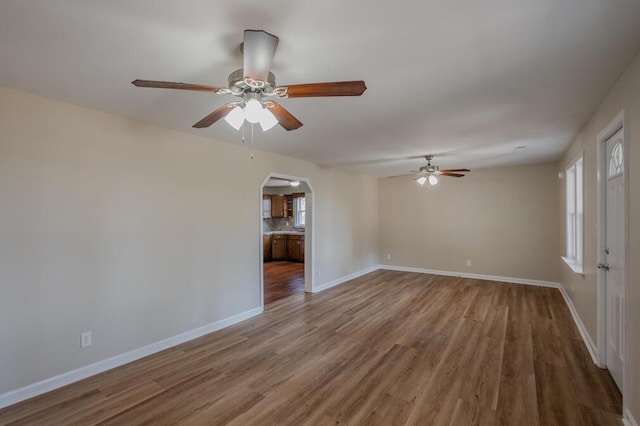 empty room with arched walkways, baseboards, a ceiling fan, and wood finished floors