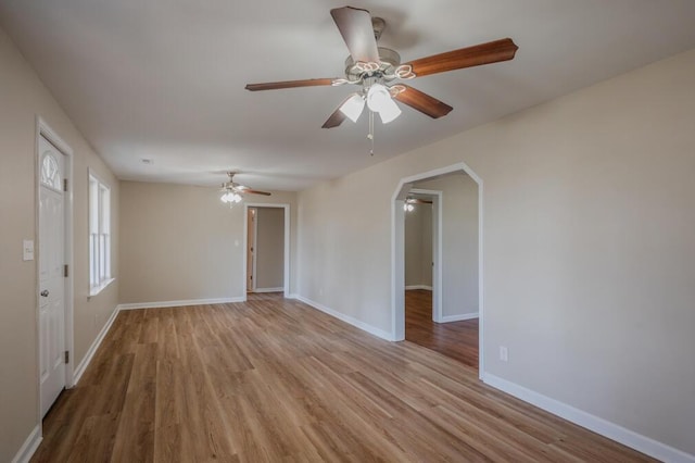 spare room with a ceiling fan, wood finished floors, arched walkways, and baseboards