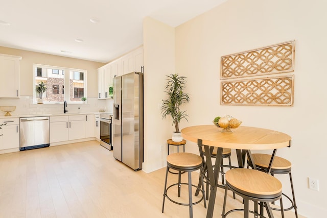 kitchen with light wood-type flooring, decorative backsplash, appliances with stainless steel finishes, white cabinets, and a sink