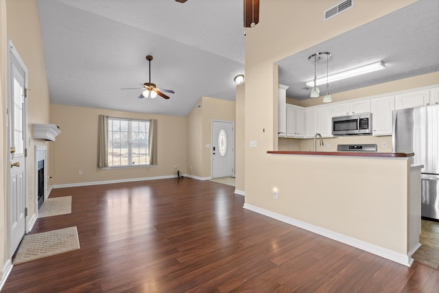 kitchen featuring visible vents, ceiling fan, a fireplace with flush hearth, dark wood-style floors, and stainless steel appliances