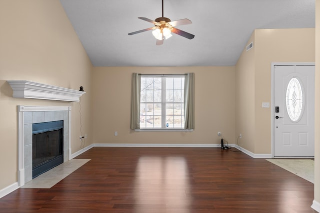 unfurnished living room with visible vents, ceiling fan, a tiled fireplace, lofted ceiling, and wood finished floors