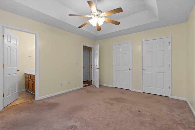 unfurnished bedroom with baseboards, a tray ceiling, ceiling fan, light carpet, and connected bathroom