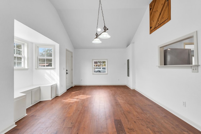 unfurnished dining area with electric panel, vaulted ceiling, baseboards, and hardwood / wood-style floors