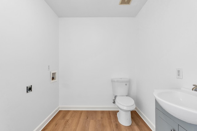 bathroom featuring visible vents, baseboards, toilet, wood finished floors, and vanity