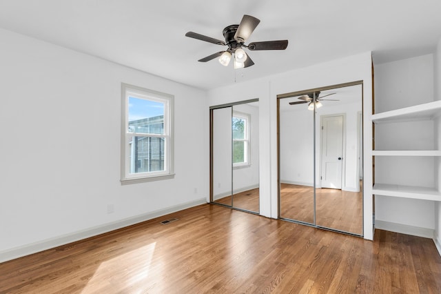 unfurnished bedroom with baseboards, wood finished floors, visible vents, and multiple closets