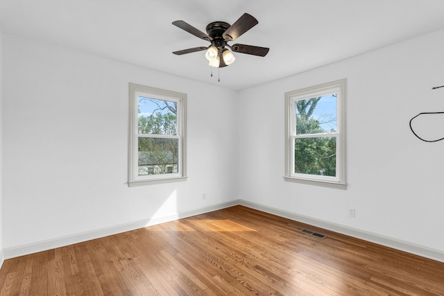 unfurnished room with visible vents, a healthy amount of sunlight, baseboards, and wood finished floors