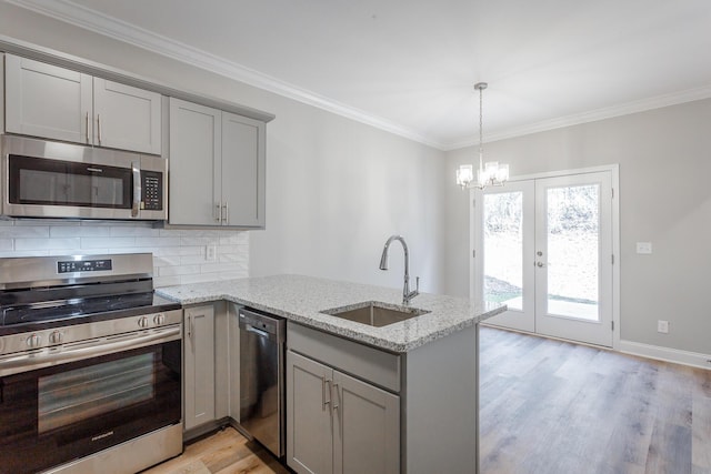 kitchen with a peninsula, gray cabinets, a sink, appliances with stainless steel finishes, and crown molding