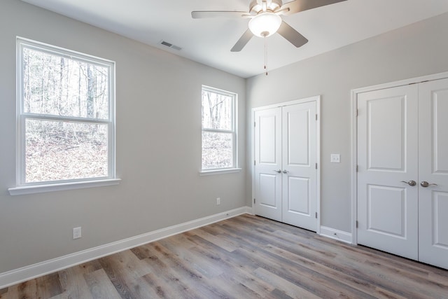 unfurnished bedroom with wood finished floors, visible vents, multiple closets, and baseboards