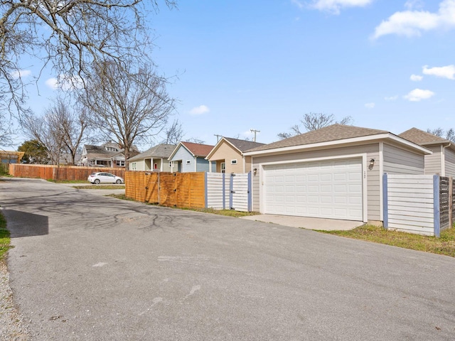 single story home featuring a detached garage, a gate, fence, and a residential view